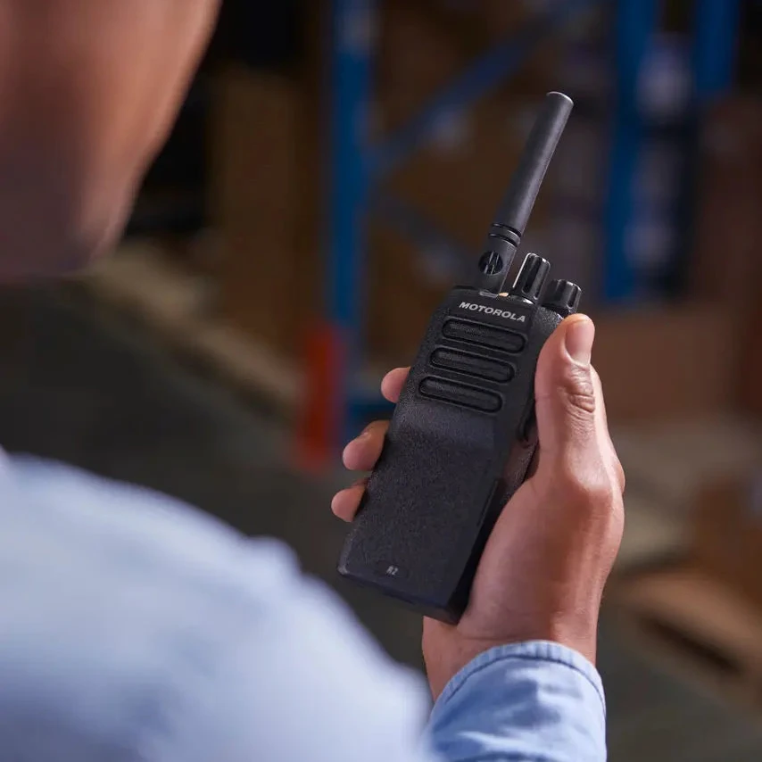 A person in a warehouse holding a black Motorola two-way radio walkie-talkie in their hand, shown from an over-the-shoulder perspective.